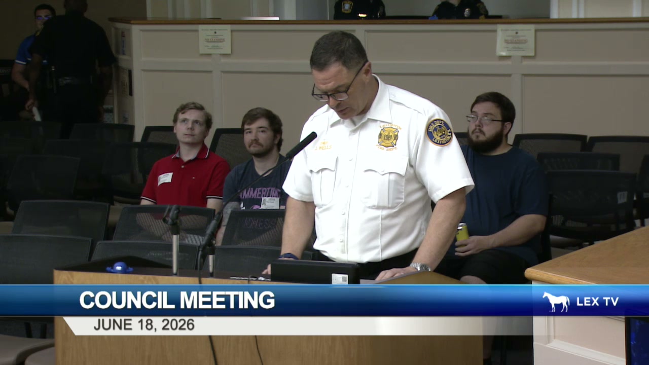 Fire Chief Jason Wells in a white uniform shirt speaking at the podium in the Urban County Council chamber