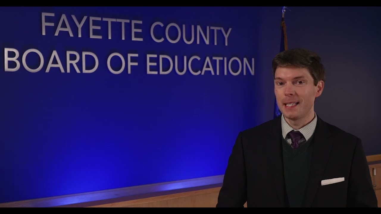 Tyler Murphy speaking to camera in front of the Fayette County Board of Education wall seal