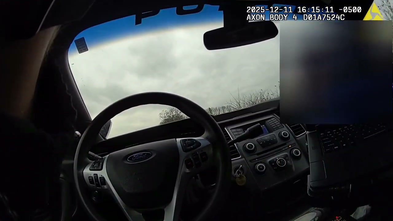 View from inside a police cruiser showing the steering wheel and dashboard, with a section of the frame blurred by the department