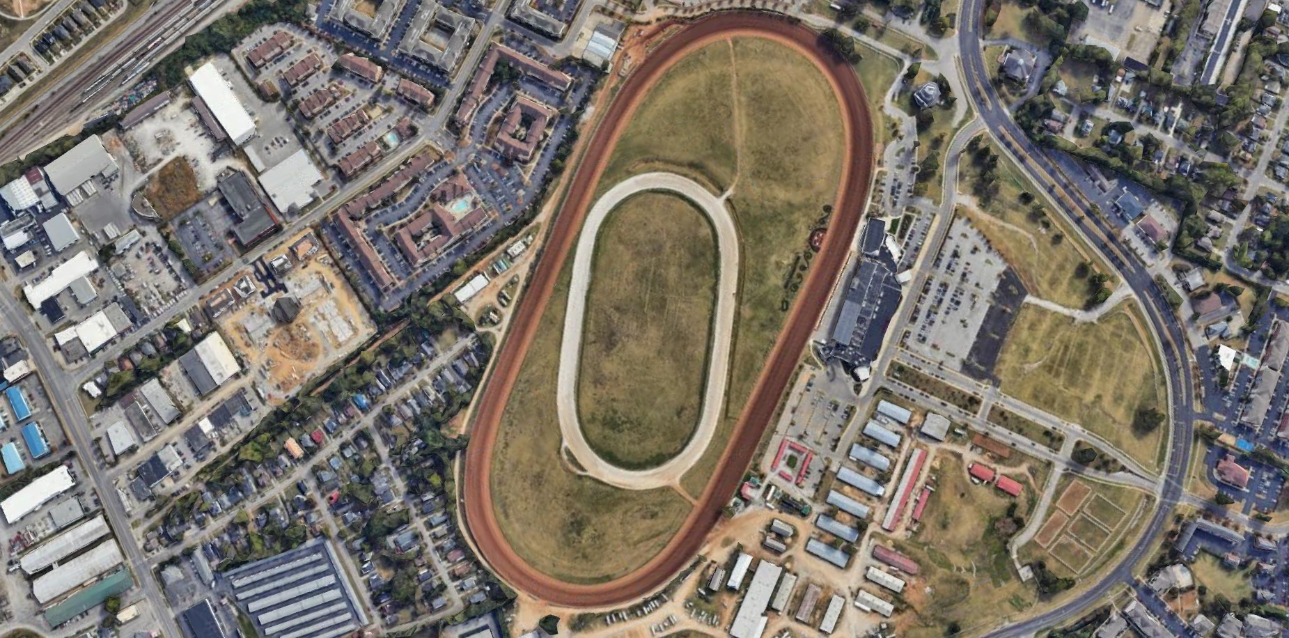 Overhead aerial of the Red Mile harness track showing the dirt oval, grass infield, inner training track, grandstand and barns, surrounded by Lexington development
