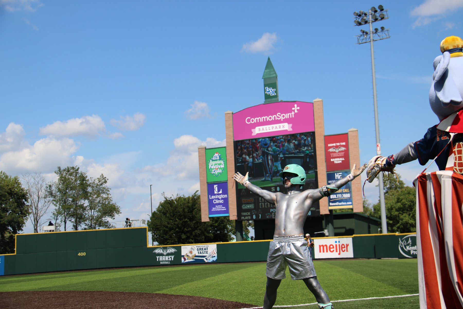 The silver-painted Coconut celebrates on the warning track under the CommonSpirit Ballpark scoreboard.